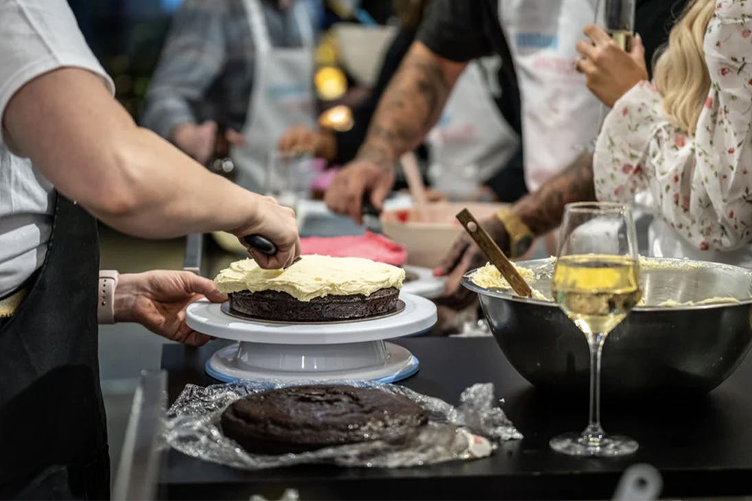 a person icing a cake with a glass of wine nearby